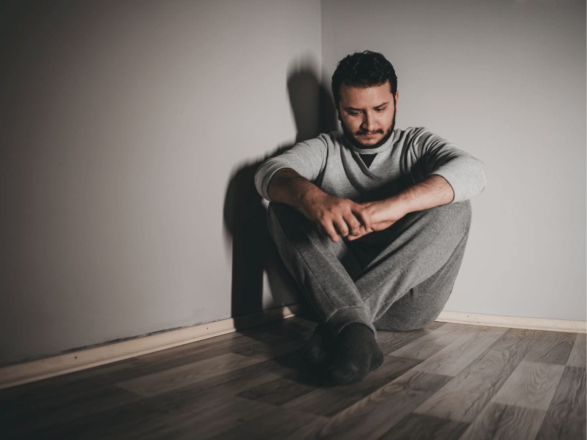 a depressed man sitting in a corner of a room